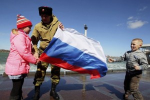 Un hombre ataviado con pantalones de camuflaje y botas militares sostiene una bandera de Rusia junto