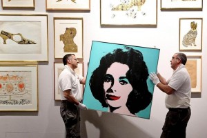 Dos hombres cuelgan el retrato de Liz Taylor del artista estadounidense, Andy Warhol, como preparaci