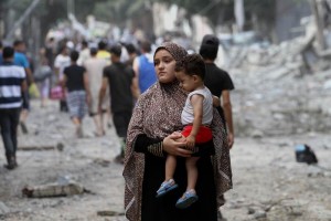  Una palestina sostiene a su hijo mientras camina frente a las viviendas destruidas despus de un at